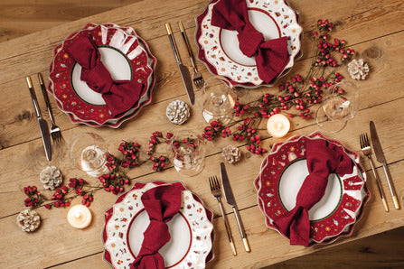 Four Toys Delight deep plates in red multi set on wooden table with red napkins, candles, and berry garland