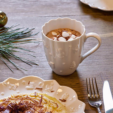 Angled view of Royal Classic mug in white showing scalloped rim and embossed holiday motifs, filled with cocoa and marshmallows