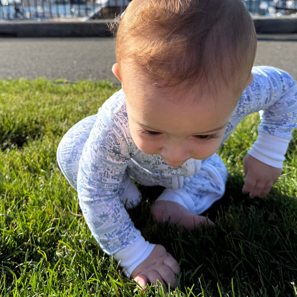 Front view of Tennis Zip Baby Onesie showcasing its hand-drawn tennis print on a baby crawling on grass
