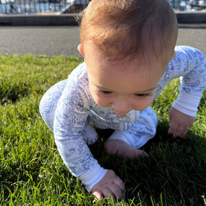 Front view of Tennis Zip Baby Onesie showcasing its hand-drawn tennis print on a baby crawling on grass