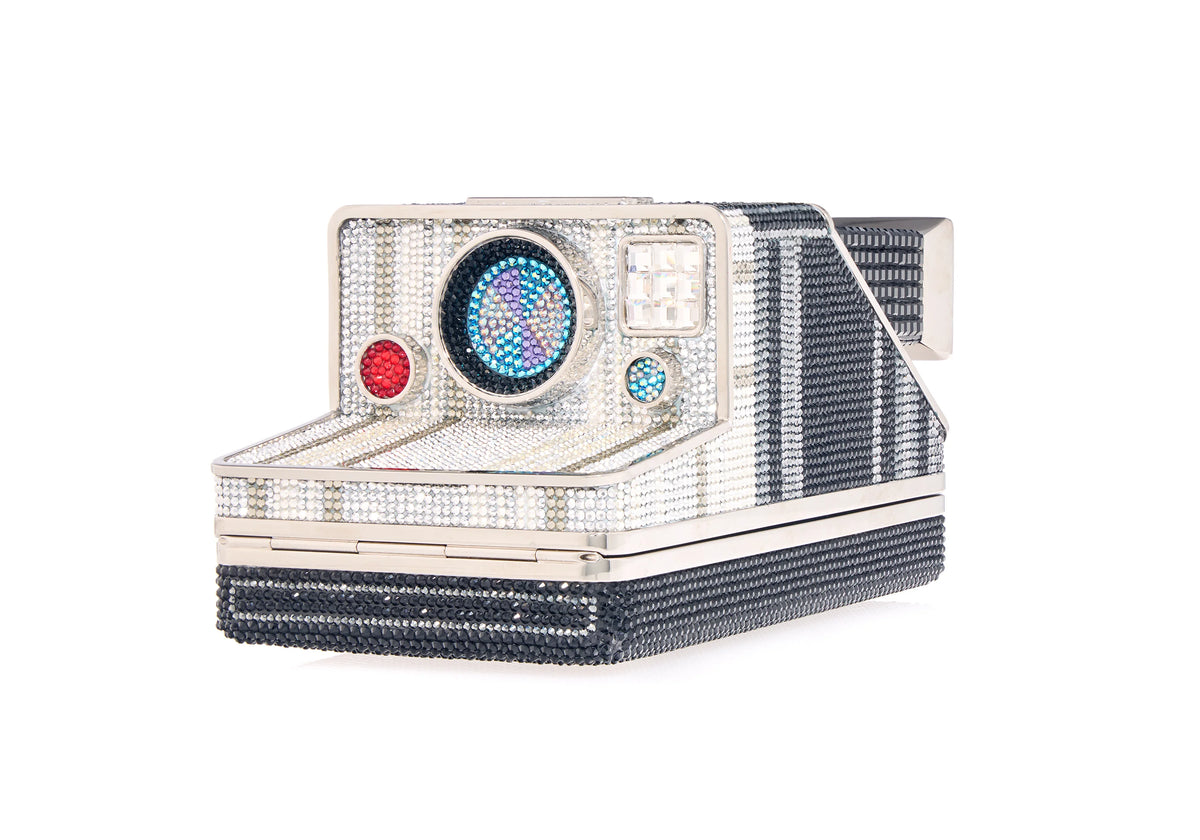 Angled view of Judith Leiber Image Elsa crystal camera clutch with multicolored lens and silver hardware on white background