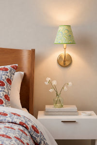 Seaglass peacock sconce illuminated on wall over nightstand