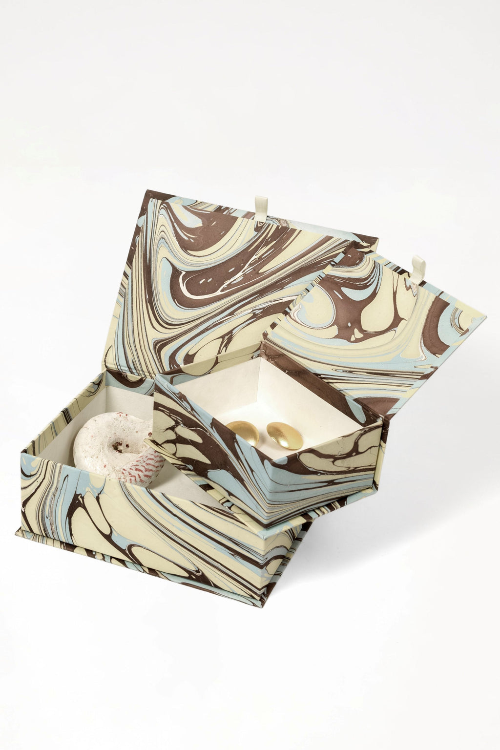 Hand-marbled keepsake box set in Kyoto with swirling brown, beige, and light blue patterns, open to reveal a speckled stone and two gold-toned items inside.