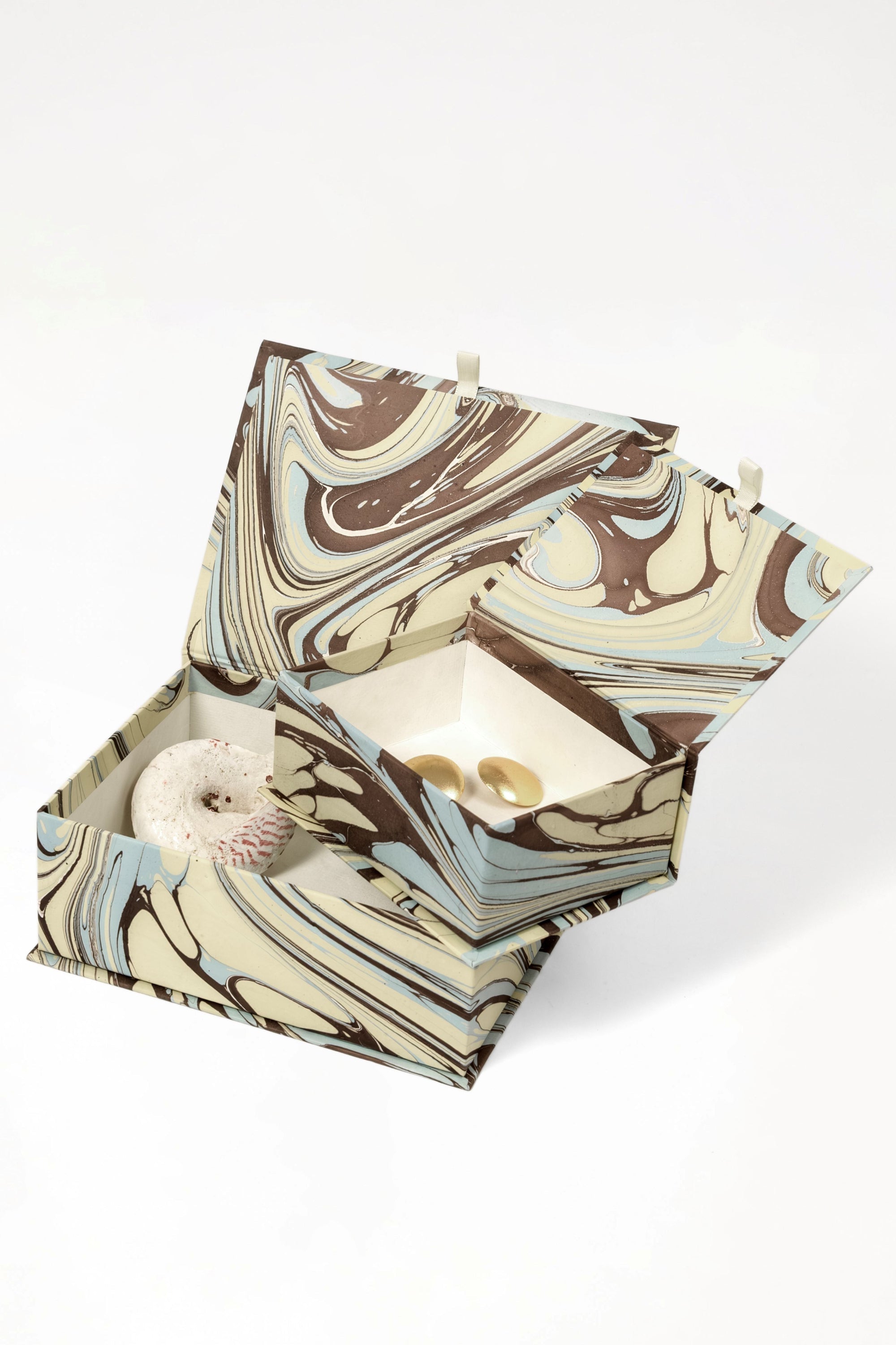 Hand-marbled keepsake box set in Kyoto with swirling brown, beige, and light blue patterns, open to reveal a speckled stone and two gold-toned items inside.
