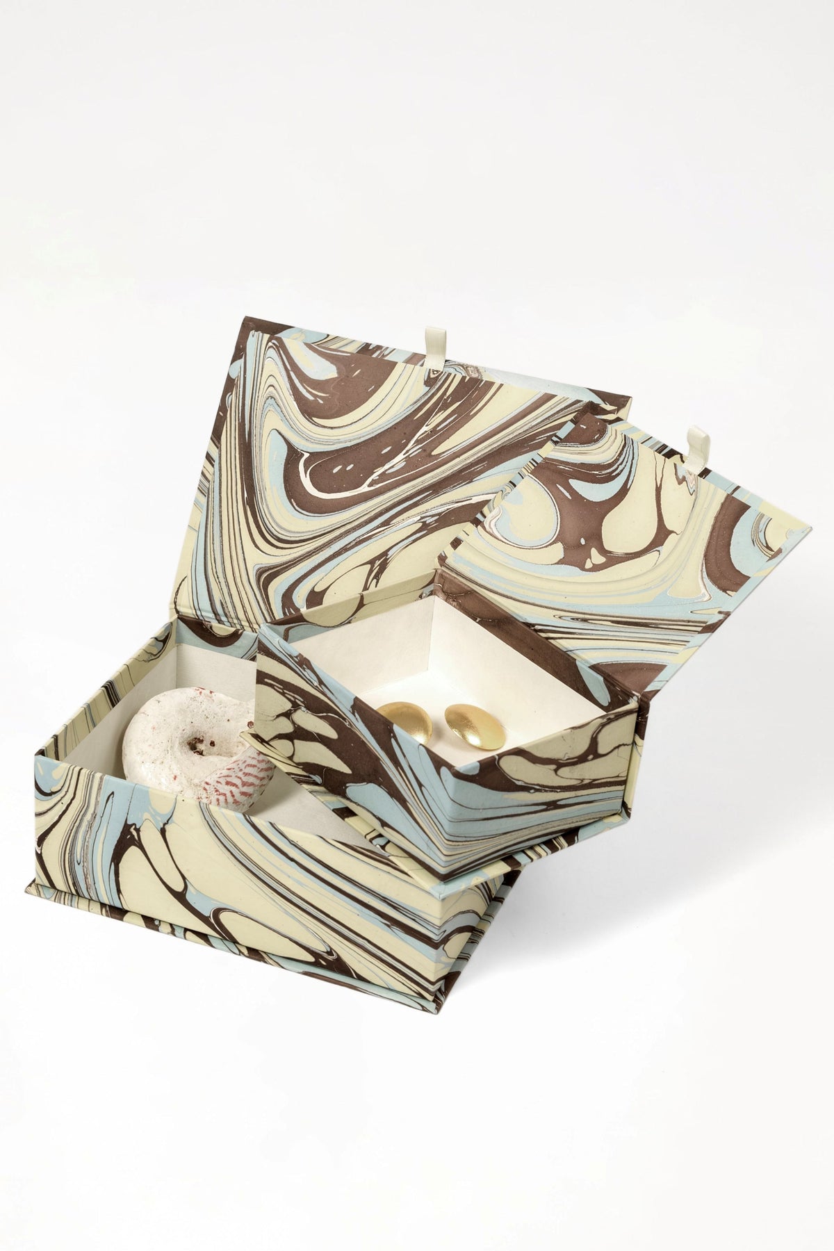 Hand-marbled keepsake box set in Kyoto with swirling brown, beige, and light blue patterns, open to reveal a speckled stone and two gold-toned items inside.