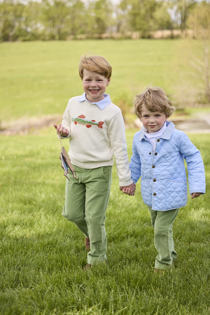 Little English traditional children's clothing.  Boys cream crew neck sweater with fish motif layered over light blue striped polo and paired with watercress green corduroy pants. Little boy wearing light blue quilted jacket with watercress green corduroy pull on pants