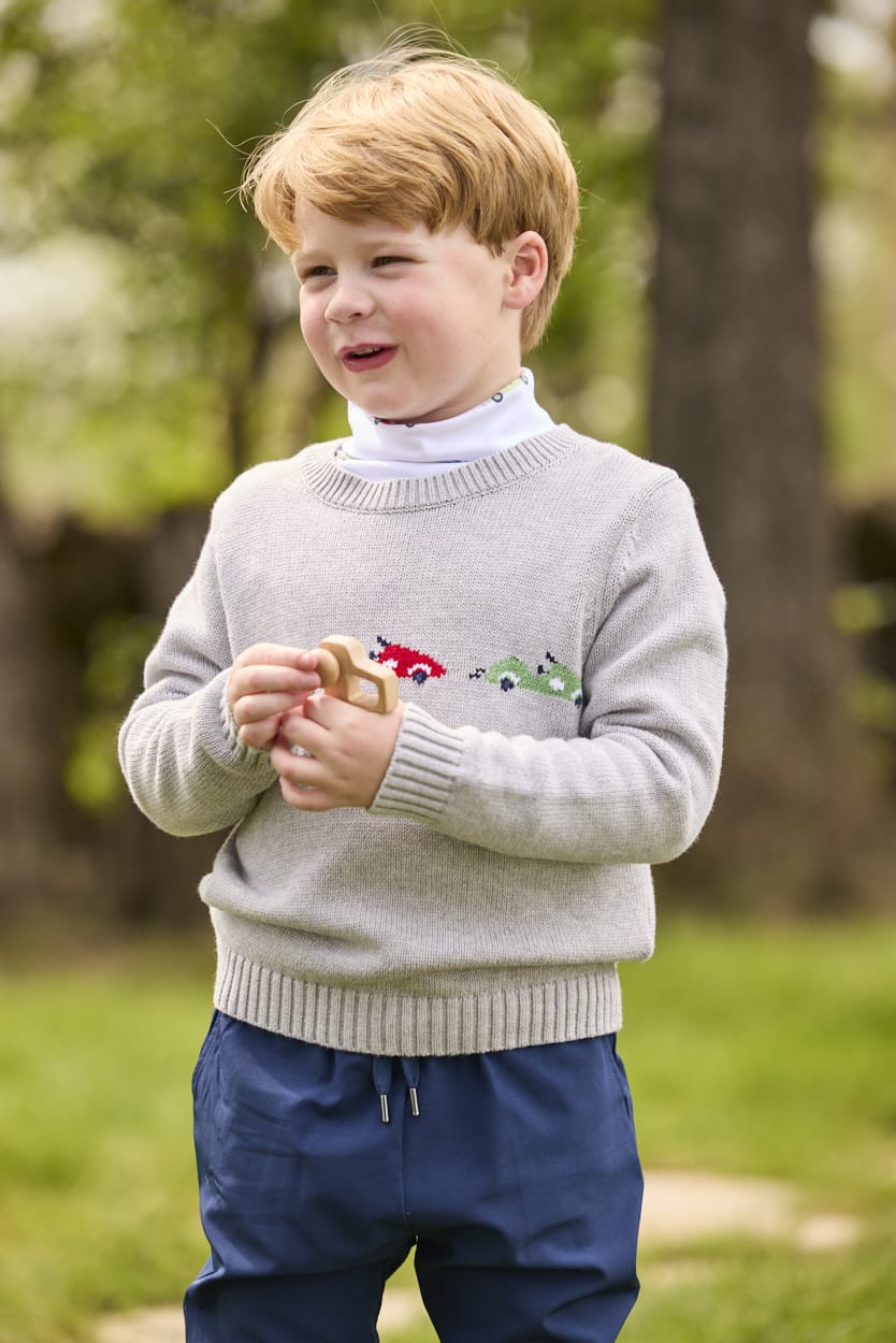 Little English traditional children's clothing.  Grey intarsia sweater with 3 race cars layered over race car print turtleneck and paired with tapered navy sport pants for little boys.