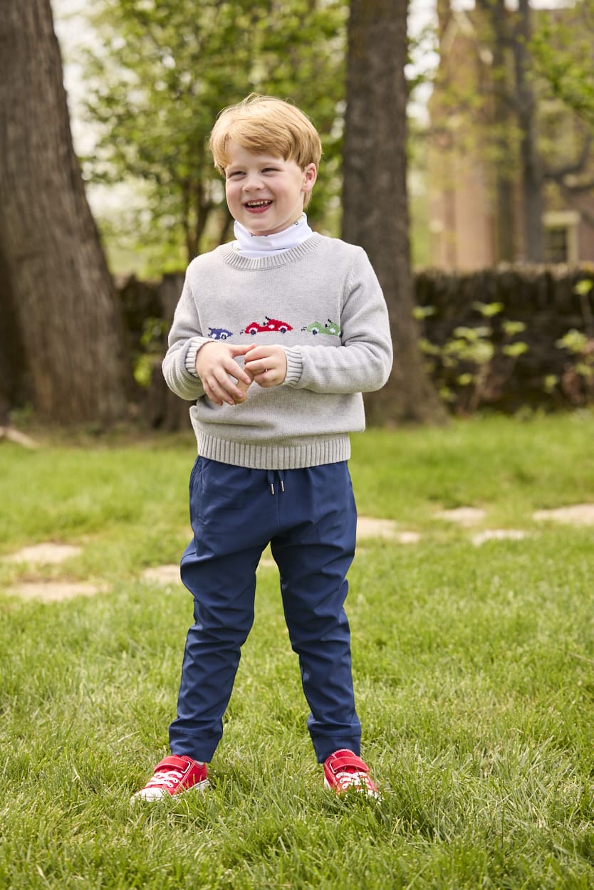 Little English traditional children's clothing.  Grey intarsia sweater with 3 race cars layered over race car print turtleneck and paired with tapered navy sport pants for little boys.