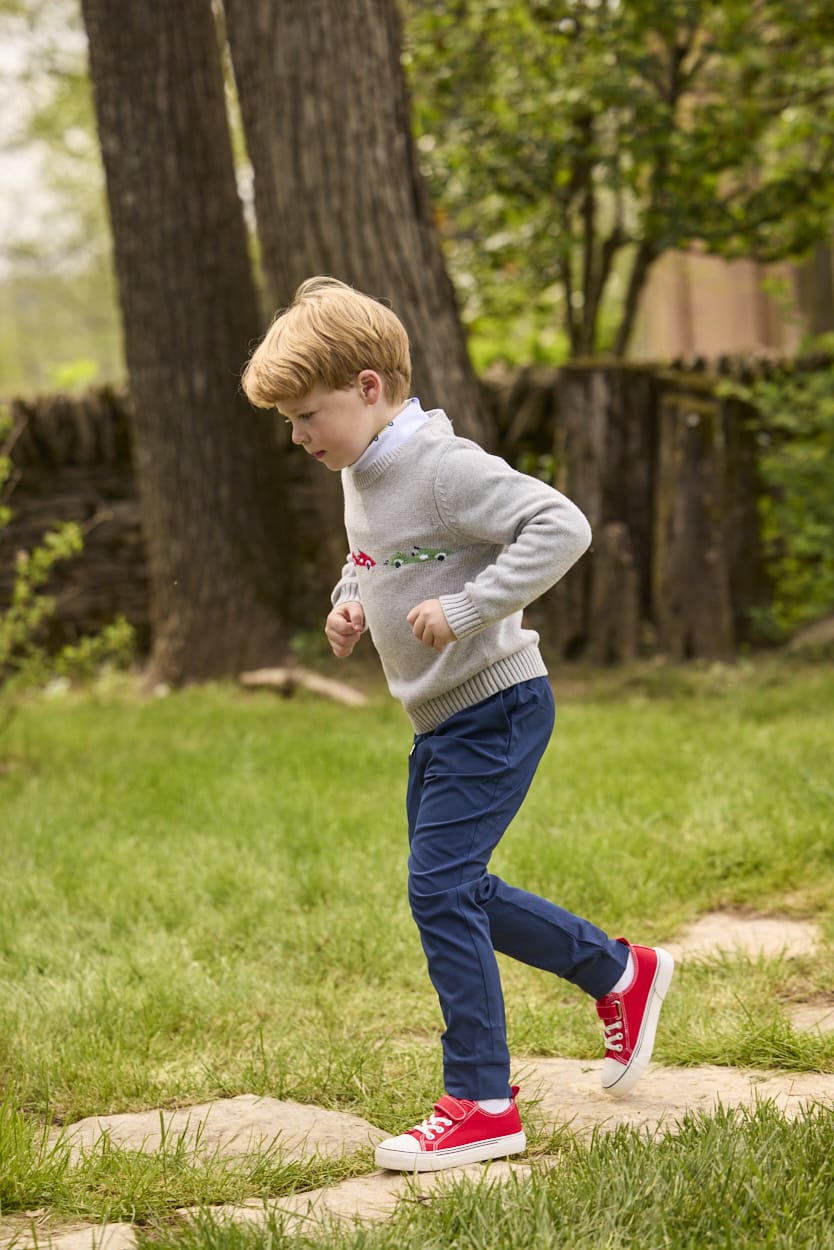 Little English traditional children's clothing.  Grey intarsia sweater with 3 race cars layered over race car print turtleneck and paired with tapered navy sport pants for little boys.