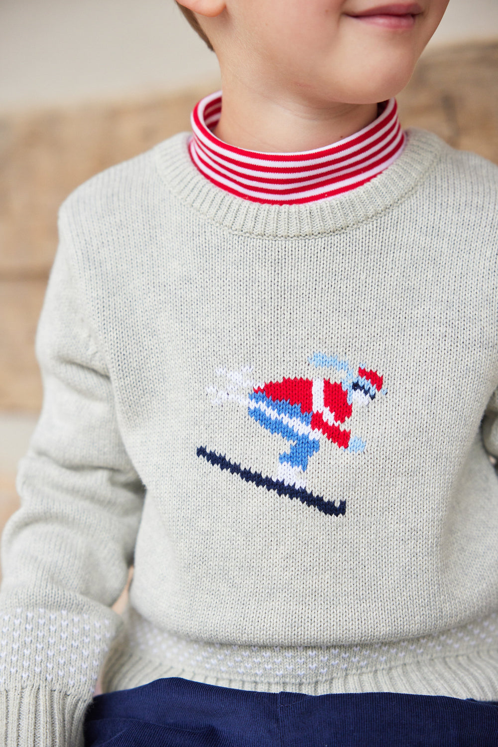Close-up of Striped Turtleneck in Red showing red-and-white striped neck worn under a light gray sweater with skier motif