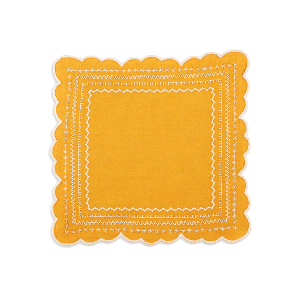 Top-down view of Isabelle napkin in mustard showcasing scalloped edges and white embroidered border on white background