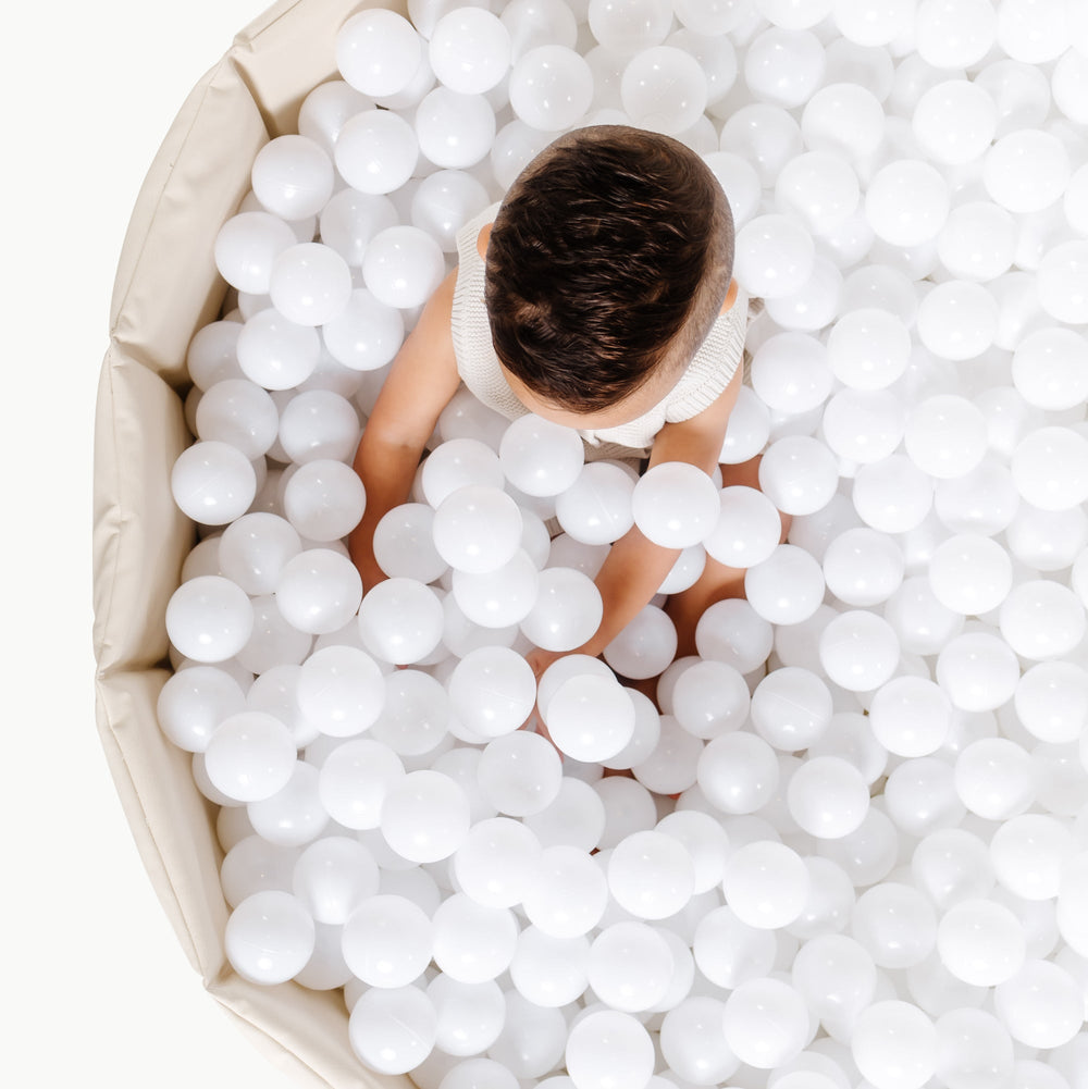 Overhead of Children’s Ball Pit in ivory showing a child seated among white play balls and the beige padded sides