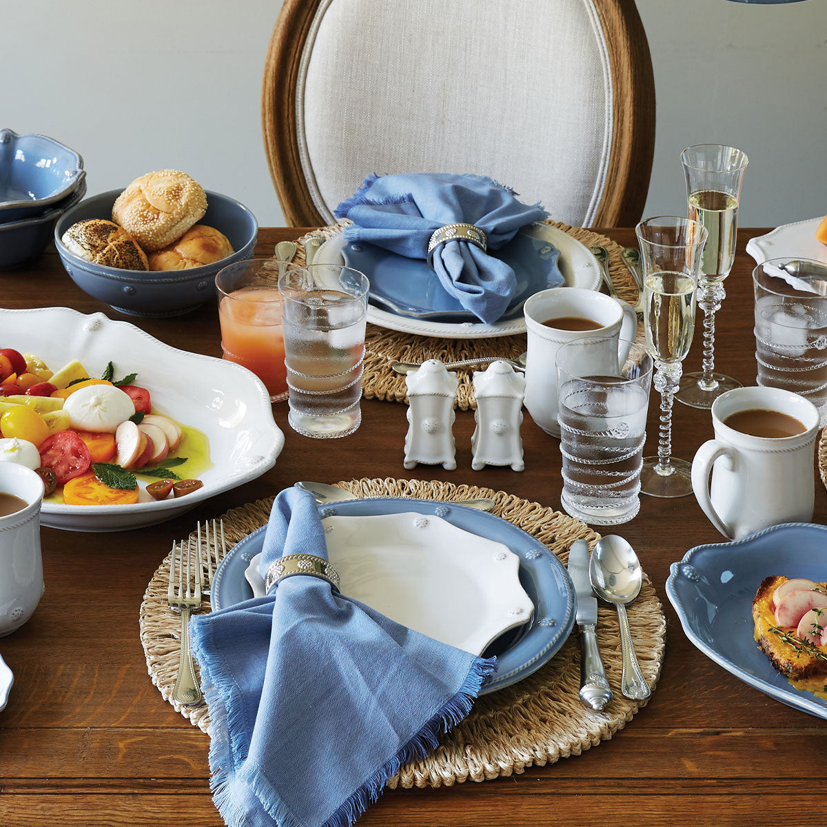 Whitewash salt and pepper shakers on a styled wooden dining table with blue plates, woven placemats, napkins, glassware, and breakfast dishes
