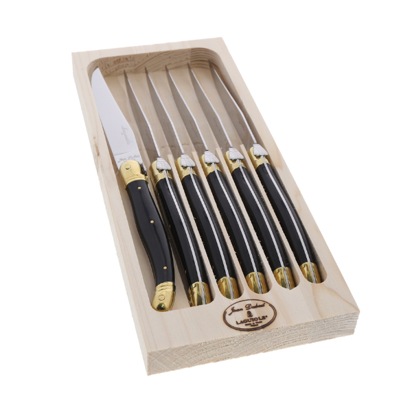 Angled view of six steak knives in a wooden tray showcasing black handles, brass detailing, and Laguiole bee emblems