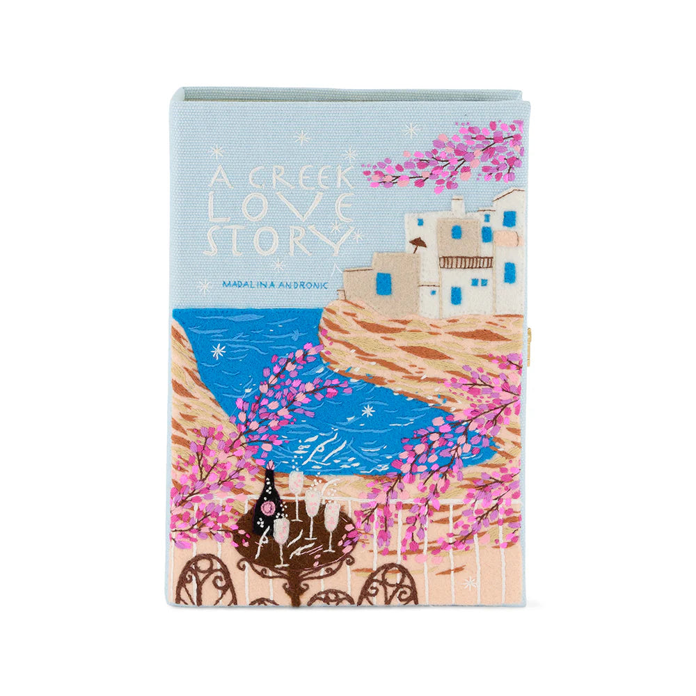 Front view of Greek Love Story book clutch with embroidered seaside book-cover design reading A Greek Love Story on white background
