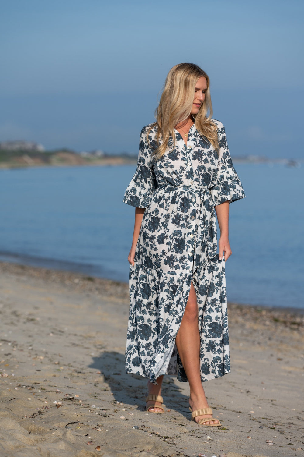 Front view of Joanna dress in Blue Dahlia on model showing bell sleeves, removable sash, button front and thigh-high slit on a beach