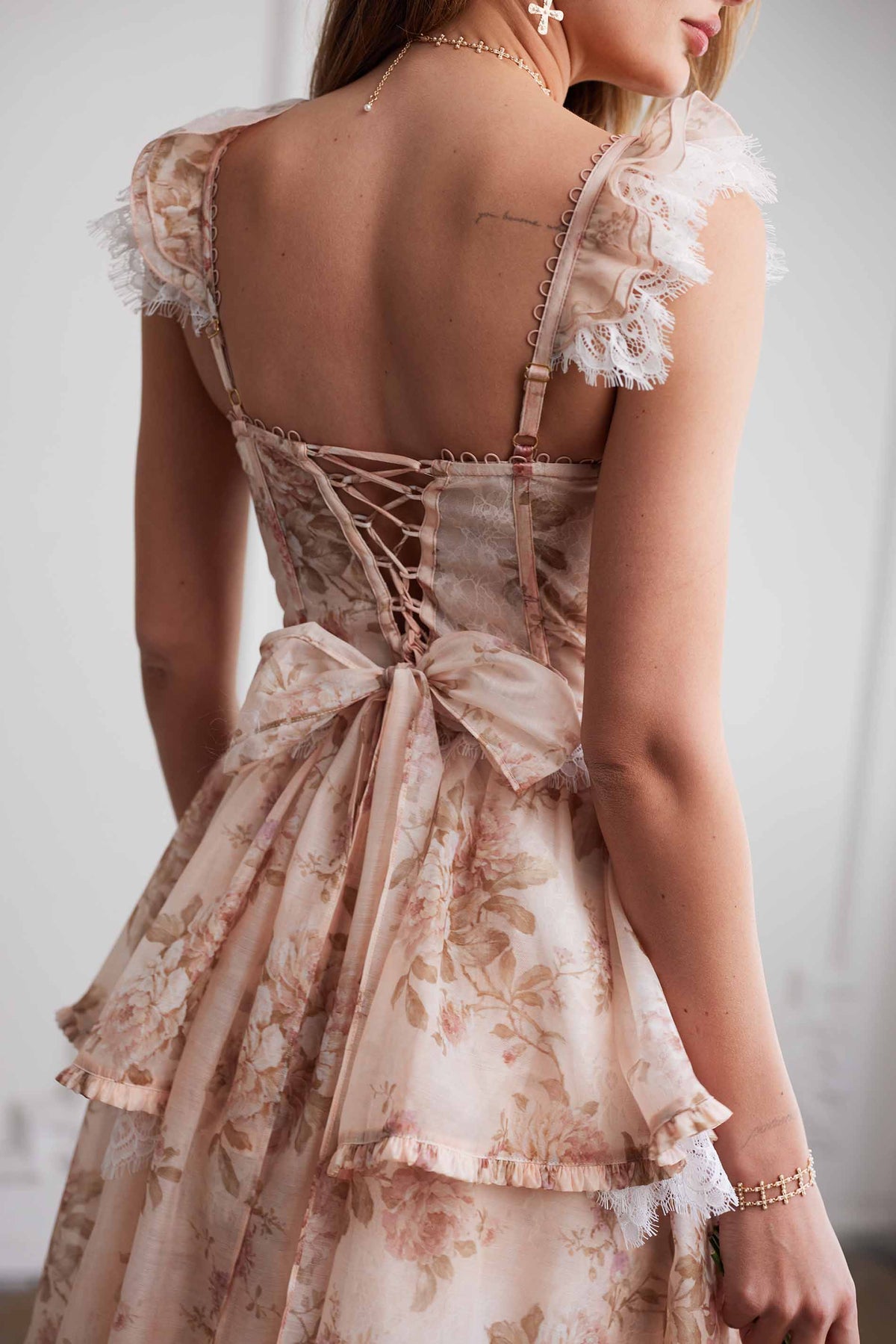 Back view of The Jolie Dress in Peach Tapestry with lace-trimmed straps, corset lacing, bow, and gray background