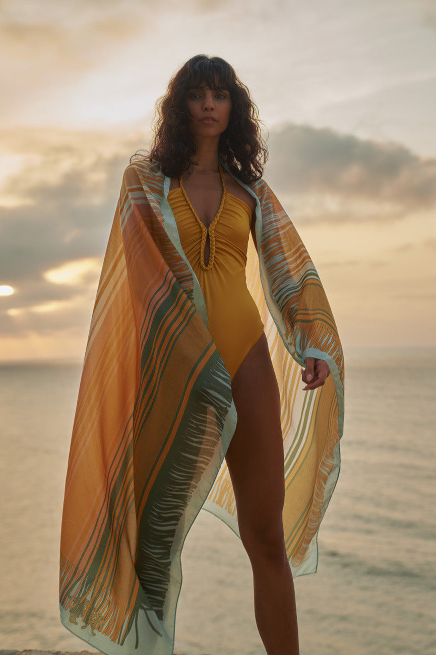 Front view of Saint Tropez One Piece in Yellow showcasing ruched neckline and hand-braided halter tie with beach background