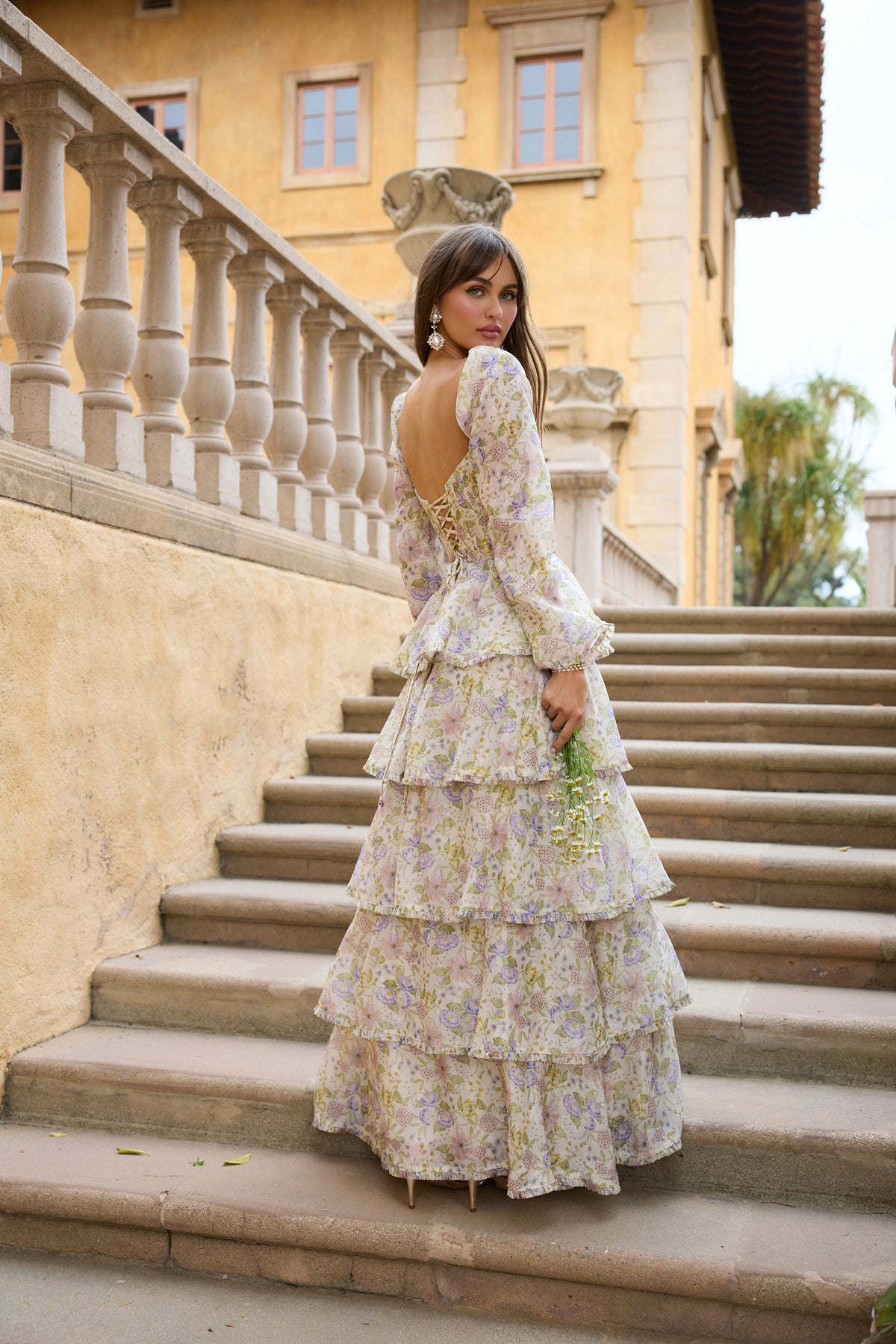 Back view of The Juliette Dress in Cordoba Print showcasing floral organza tiers and lace-up back on stone steps