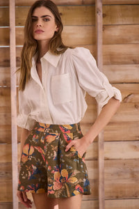 White linen long-sleeve collared shirt with roll-tab sleeves and pearl embellishments.