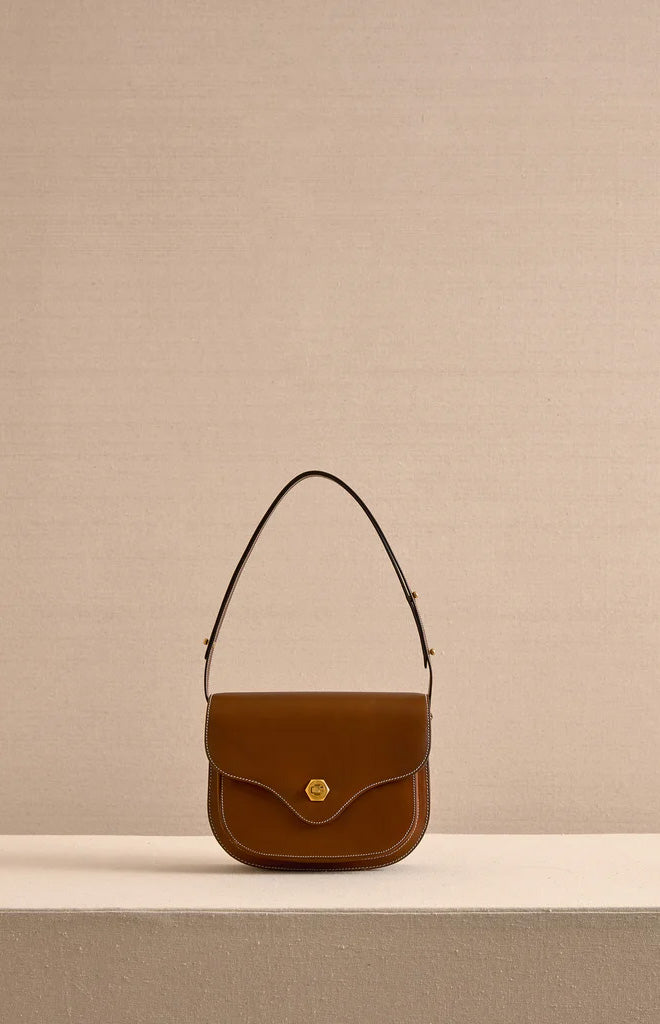 Front view of Jane shoulder bag in Acorn leather with gold clasp, white stitching, and adjustable strap on beige backdrop
