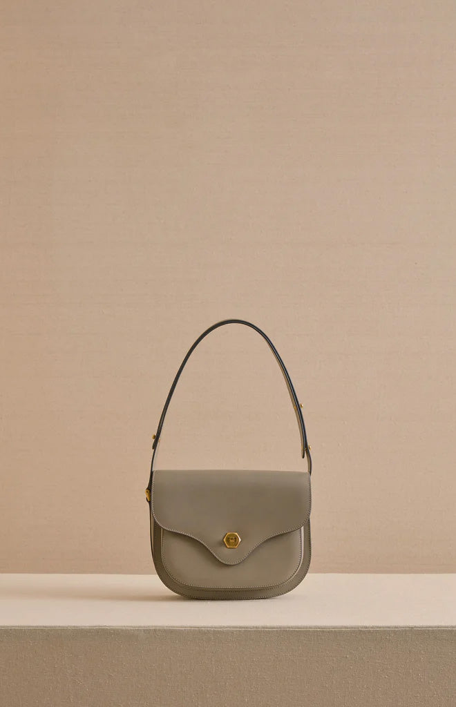 Front view of Jane shoulder bag in Vacchetta Mushroom showing curved flap, gold hex turn-lock and single top shoulder strap on beige background
