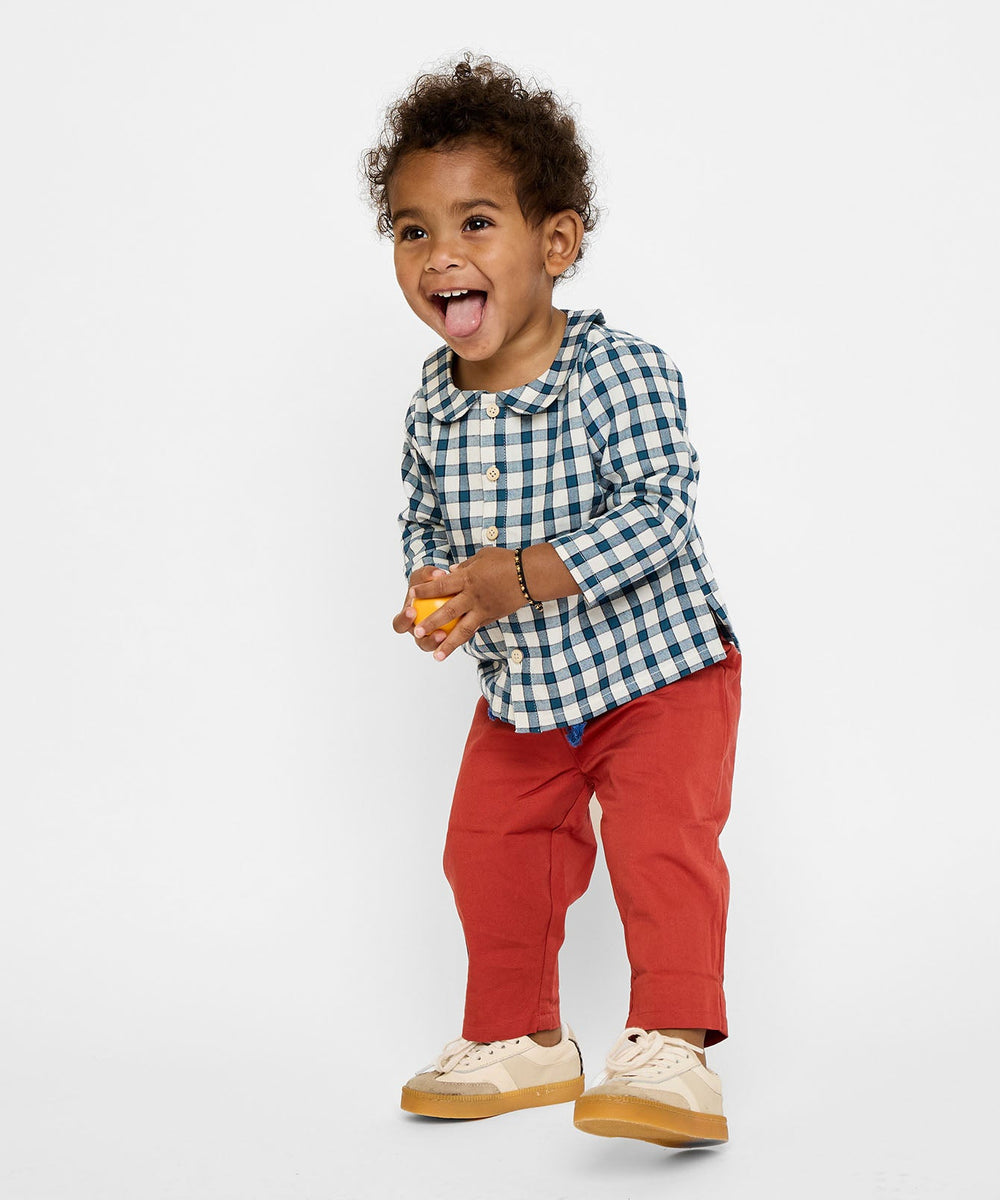 Three-quarter view of Jefferson Baby Shirt in blue picnic check on child model, showing rounded collar and button front