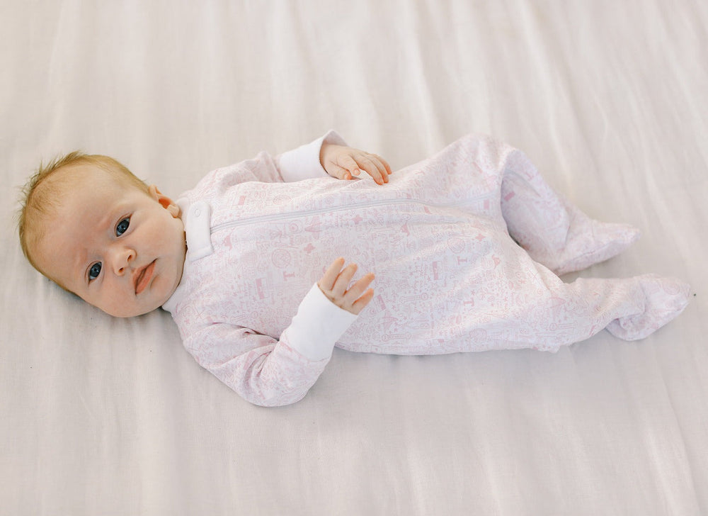 Front view of pale pink Houston zip baby onesie on infant showing full-length front zipper, white fold-over cuffs and enclosed feet on light gray sheet