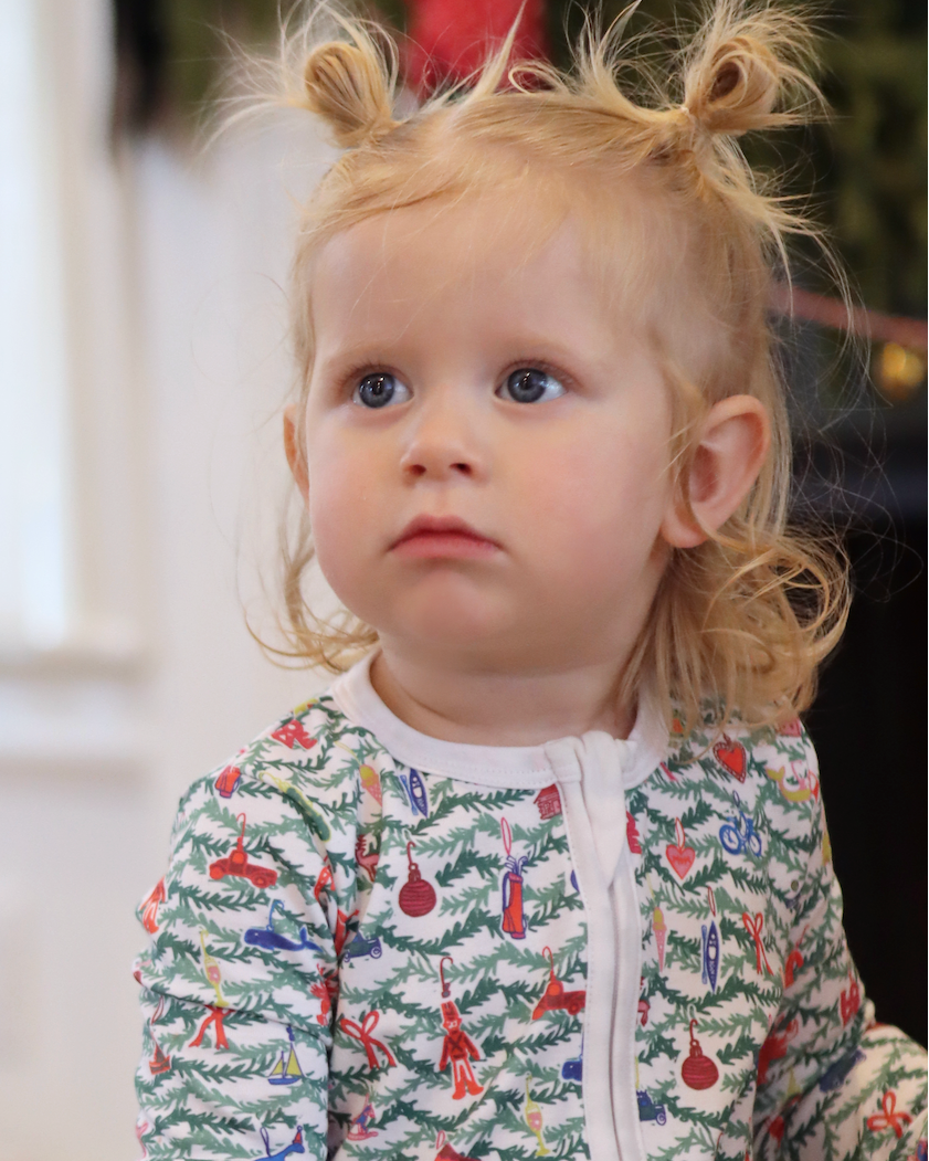 Front view of Oh Christmas Tree Zip Baby Onesie showcasing its hand-drawn evergreen and ornament print on a child indoors