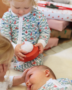 Children in Oh Christmas Tree print onesies gather around a baby beside wrapped gifts