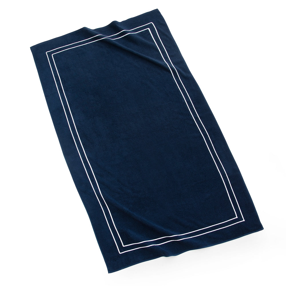 Angled top-down view of Amalfi Beach Towel showcasing navy color and double-embroidered white border on white background