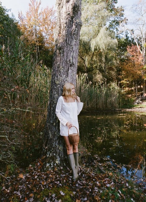 Front view of Garden Dress in white showing square neckline and long bell sleeves on model by a woodland pond