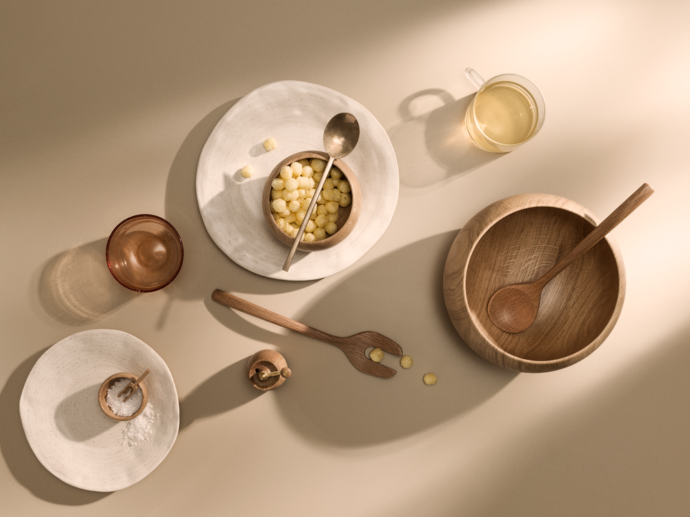 Overhead view of Kay Bojesen oak serving bowl with wooden spoon, on beige surface with plates and glass
