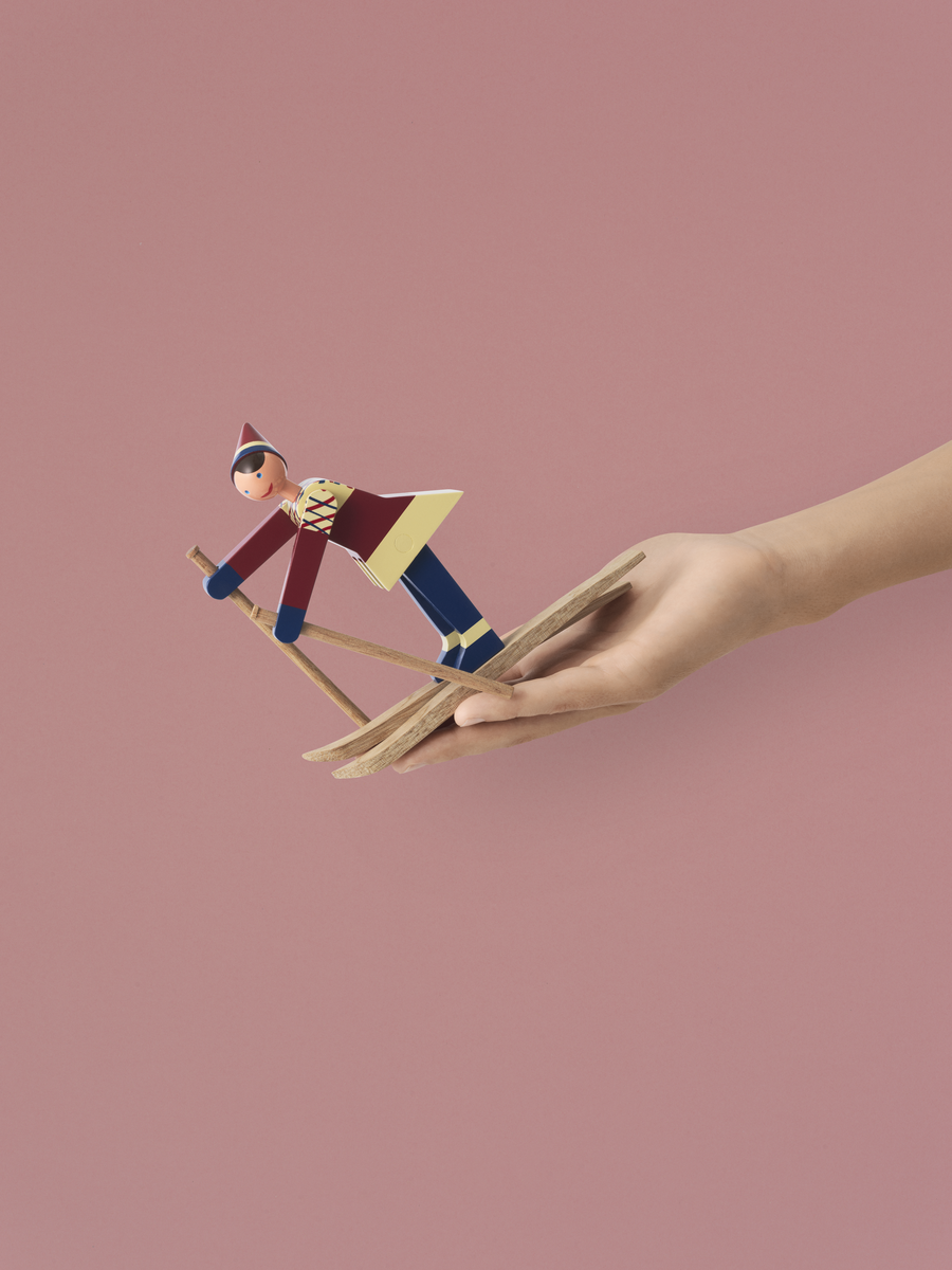 Side view of The Skier Datti in Girl Multi showcasing a painted beech skier on wooden skis against a pink background