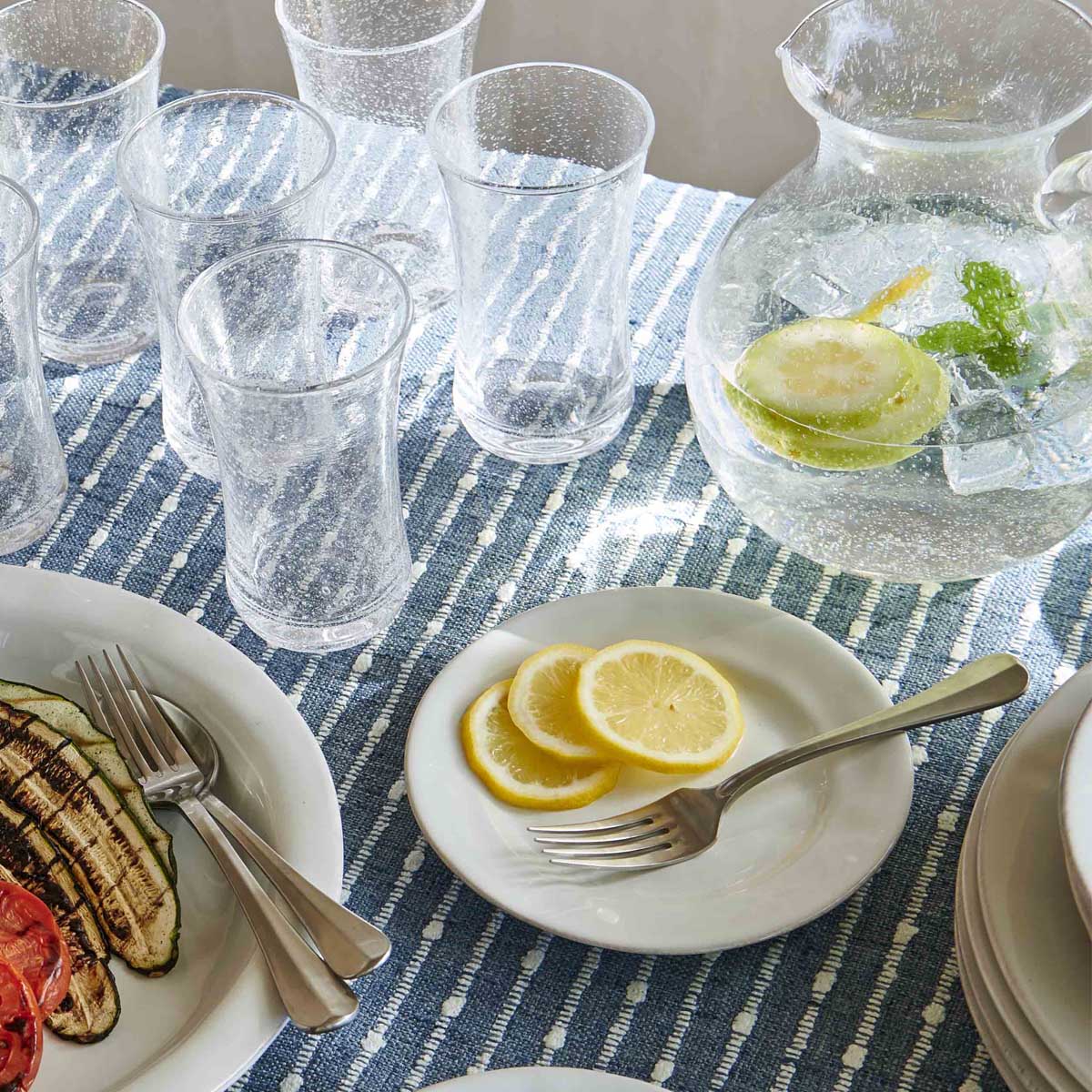 Top view of Puro Side/Cocktail Plate in Whitewash showing textured glaze with lemon slices on blue runner