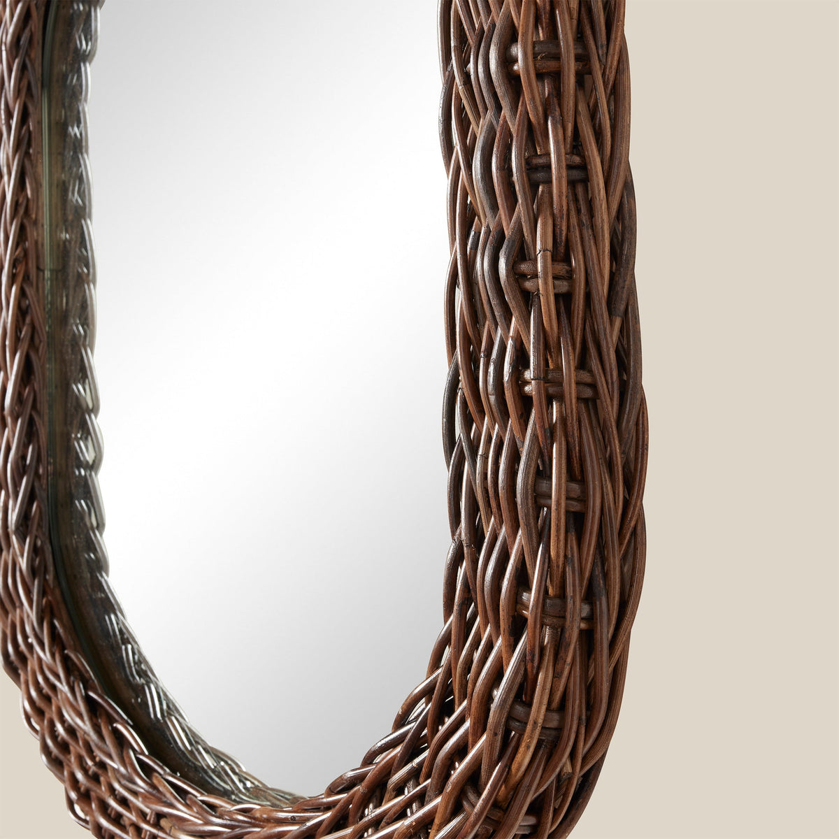 Angled view of Kingston Oval mirror showcasing woven dark brown rattan frame against a neutral beige background