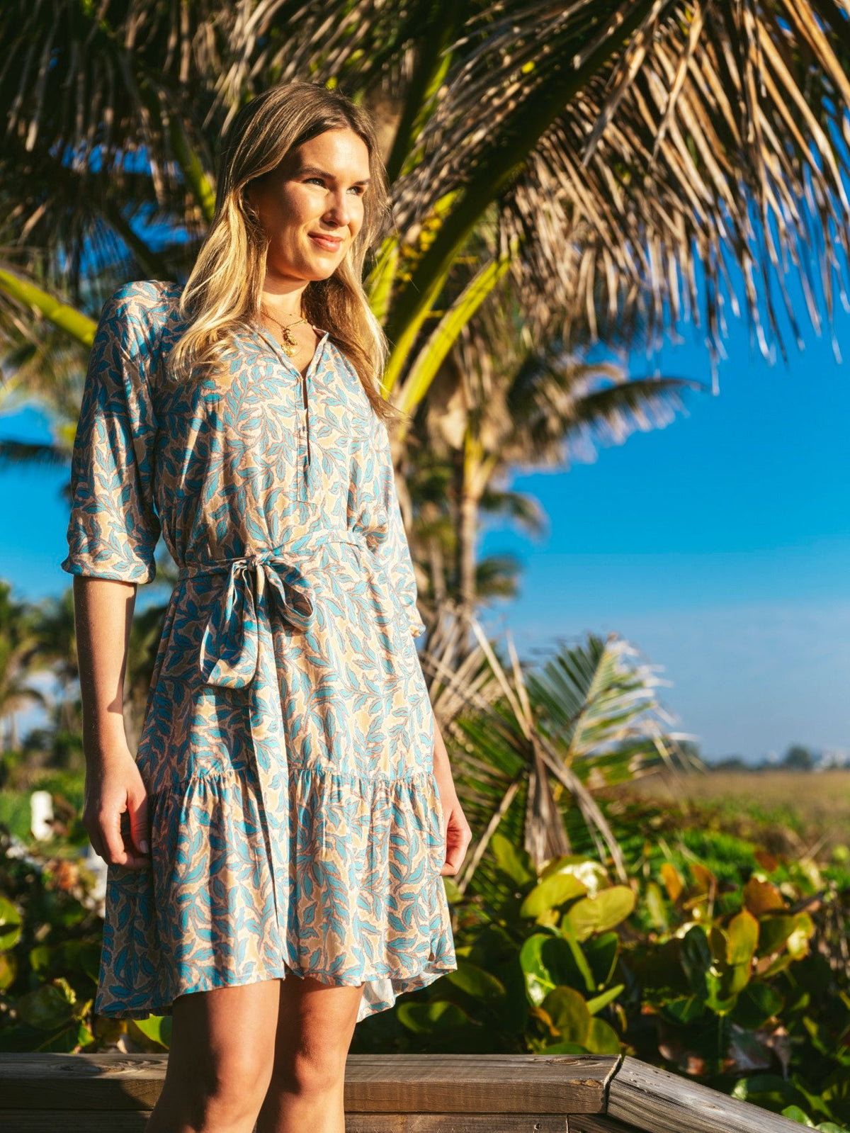 Front view of Kendall Palisades Dress showcasing blue and beige print and waist sash with palm trees in background