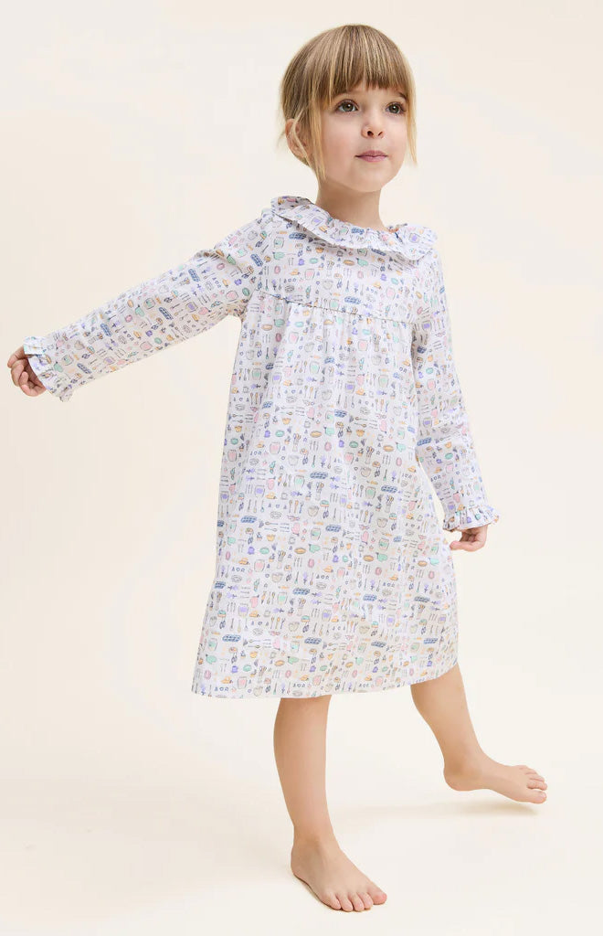 Front view of Kid’s Twill Scarlett nightgown on a child model showcasing long sleeves, ruffle collar, and pastel baking-themed print on white background