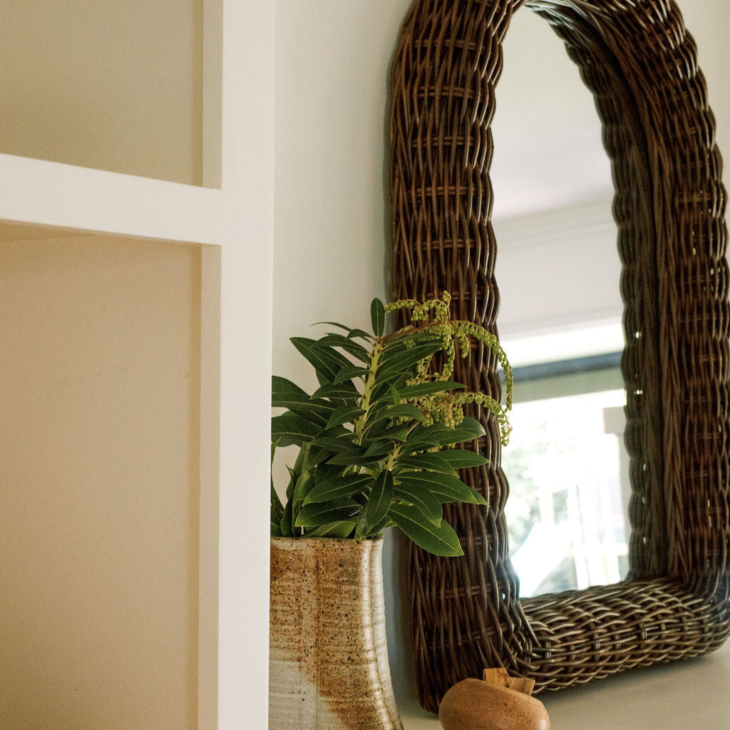 Side view of Kingston Arch Mirror showcasing woven rattan frame and arched shape beside a ceramic vase with plant