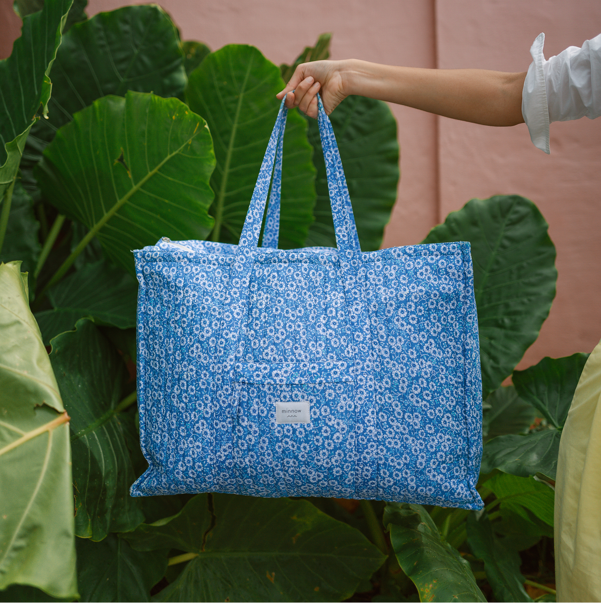 Front view of Rosebay Overnighter Tote showcasing blue floral quilted fabric, long carry handles, and exterior pocket with tropical foliage