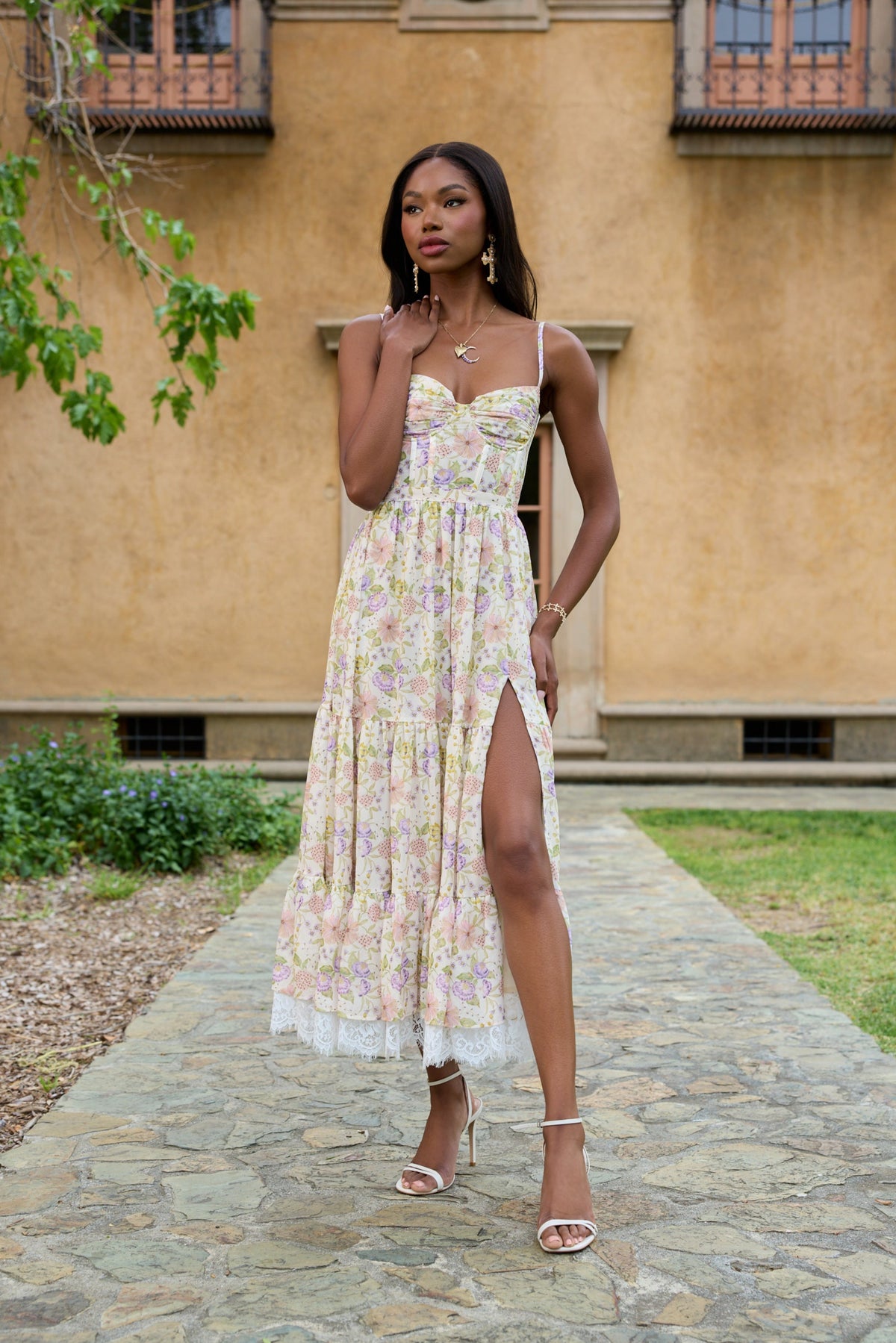 Front view of The Lara Dress in Cordoba Print showing floral chiffon tiers, lace trim, and side-front slit outdoors