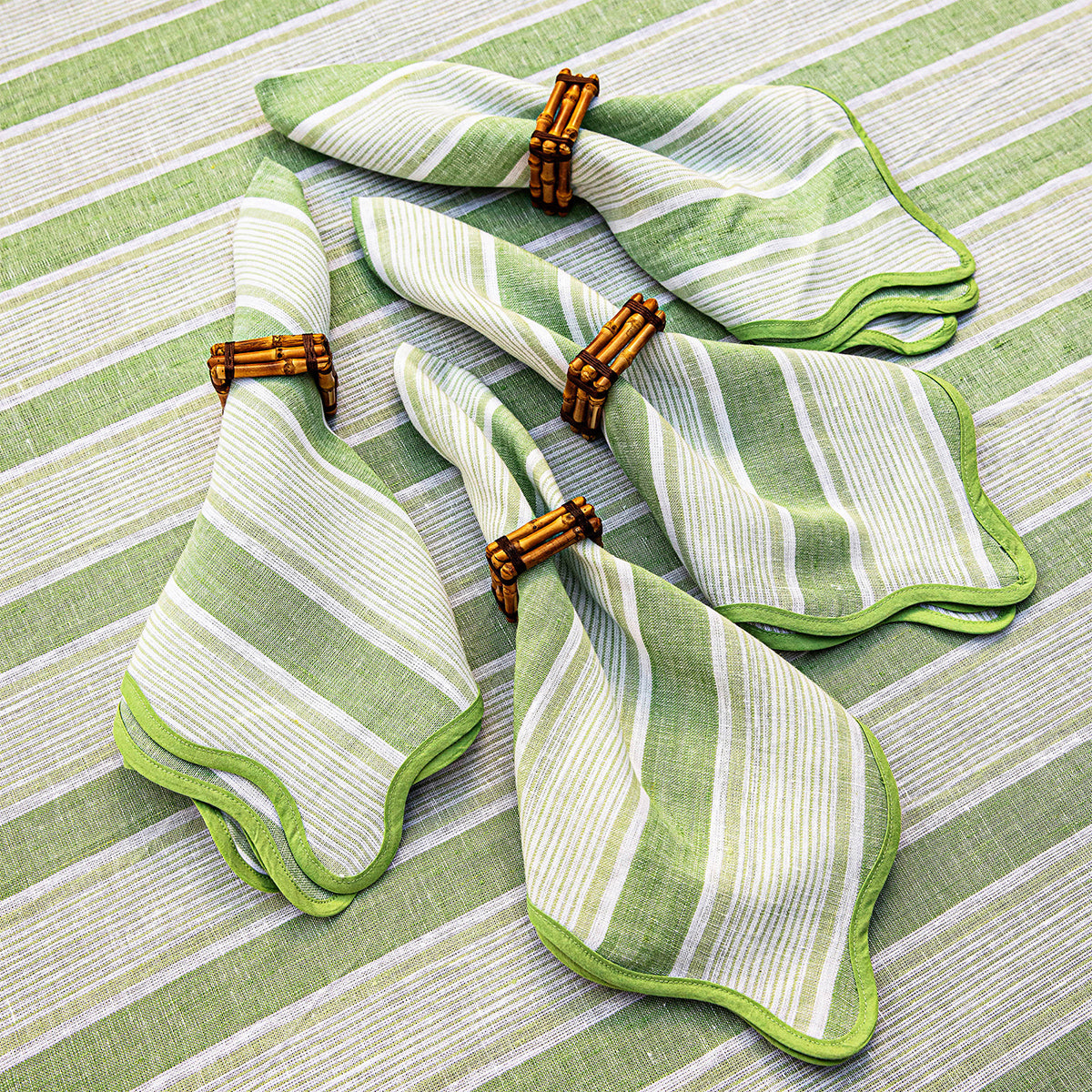 Overhead view of Cabana Stripe Napkin, Set of 4 in Seagrass showcasing scalloped trim on a striped tablecloth
