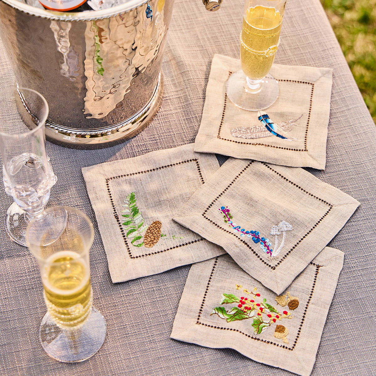 Overhead view of Forest Walk cocktail napkins, set of four, showcasing hand-embroidered woodland motifs on a table