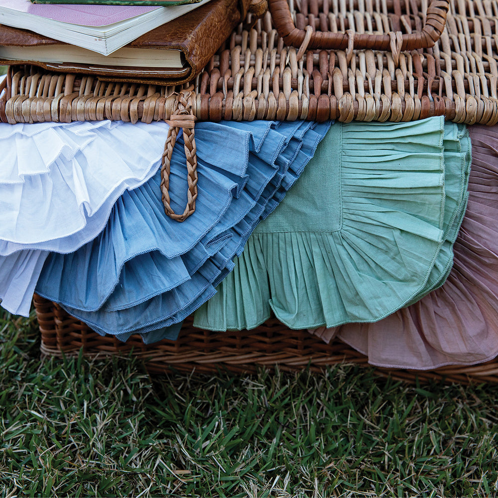Close-up of Mademoiselle napkins in chambray showing knife-pleat ruffle borders draped over a wicker picnic basket