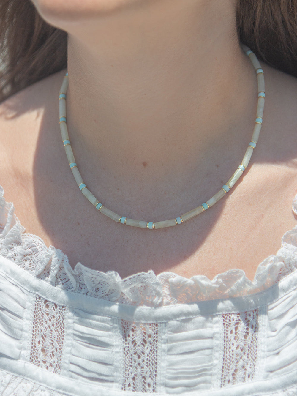 Front close-up of Libby Necklace with light-green beads and turquoise and gold spacers on a model in a white lace top