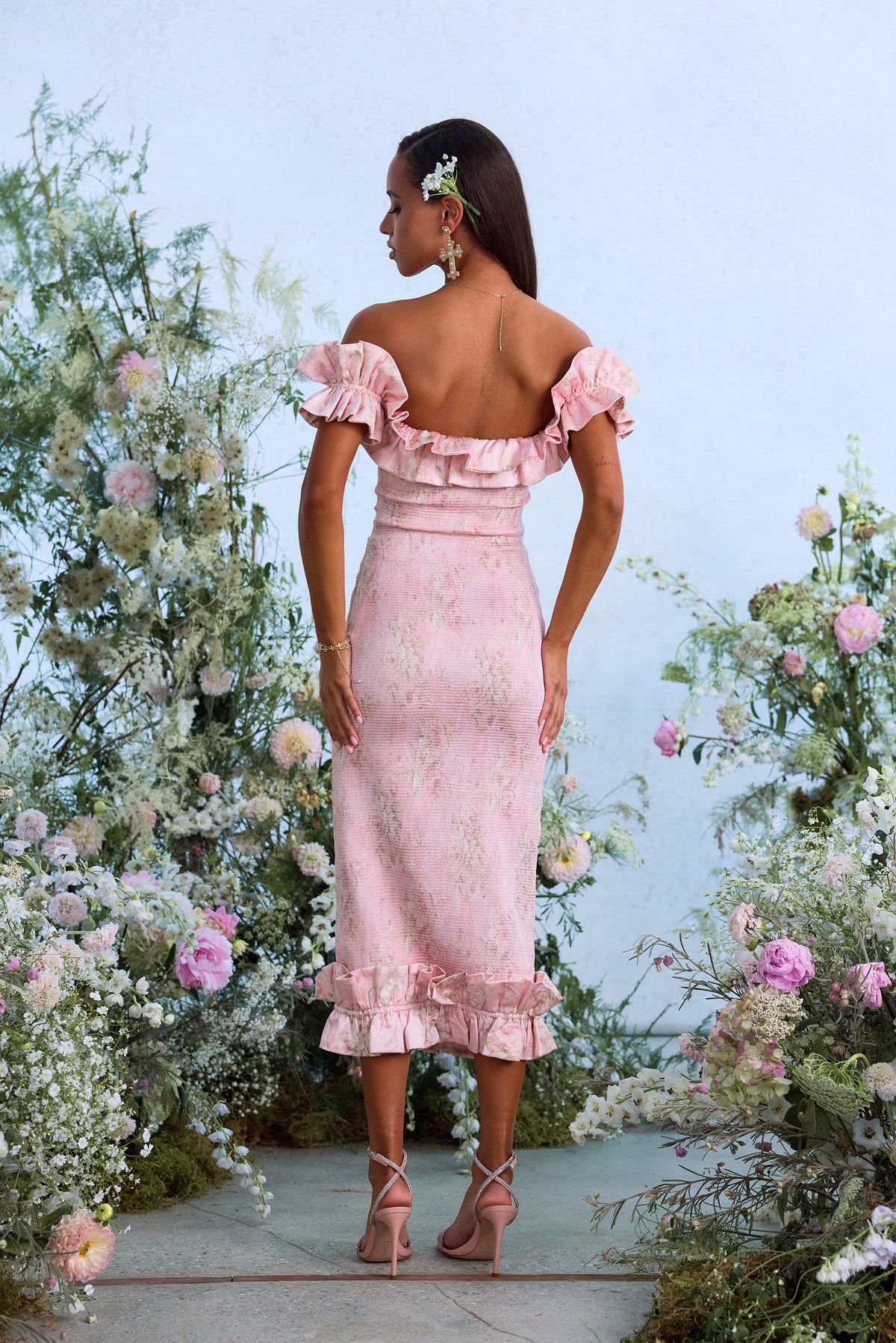 Back view of The Lilac Dress in Light Pink Tapestry Rose showcasing off-shoulder ruffles with a floral garden background