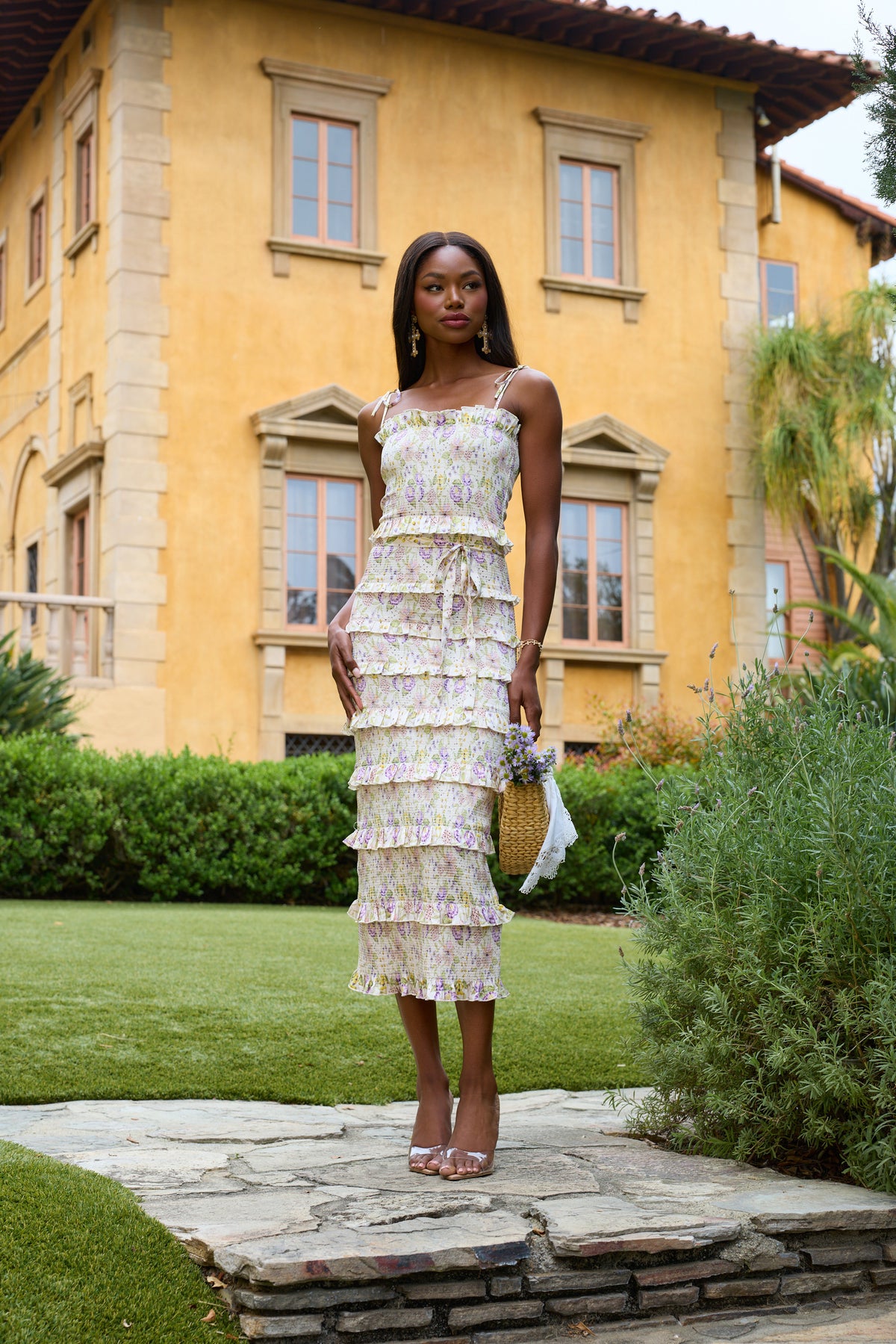 Front view of The Lily Dress in Cordoba Print showcasing multicolor floral pattern and ruffles with a garden background