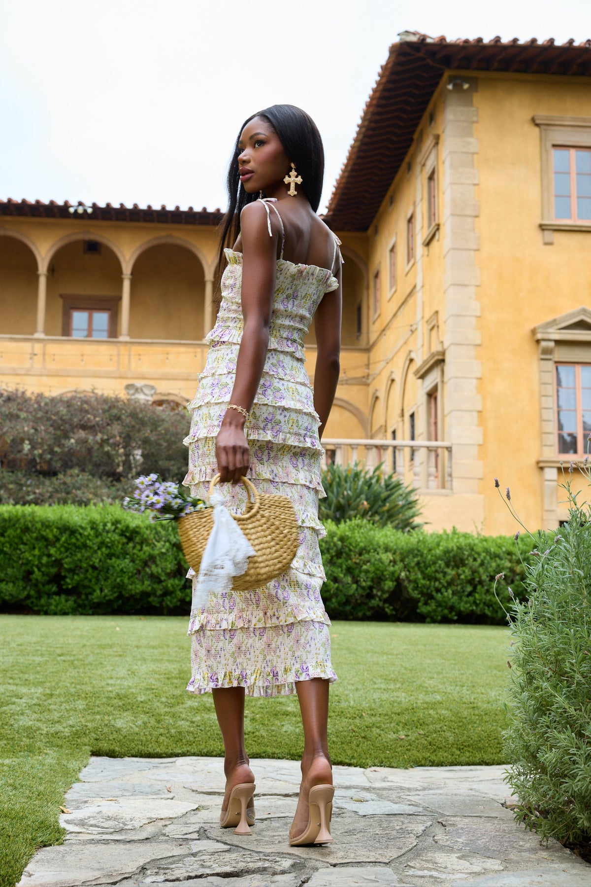 Rear three-quarter view of The Lily Dress in Cordoba Print showcasing cream multicolor floral print and ruffles in a garden