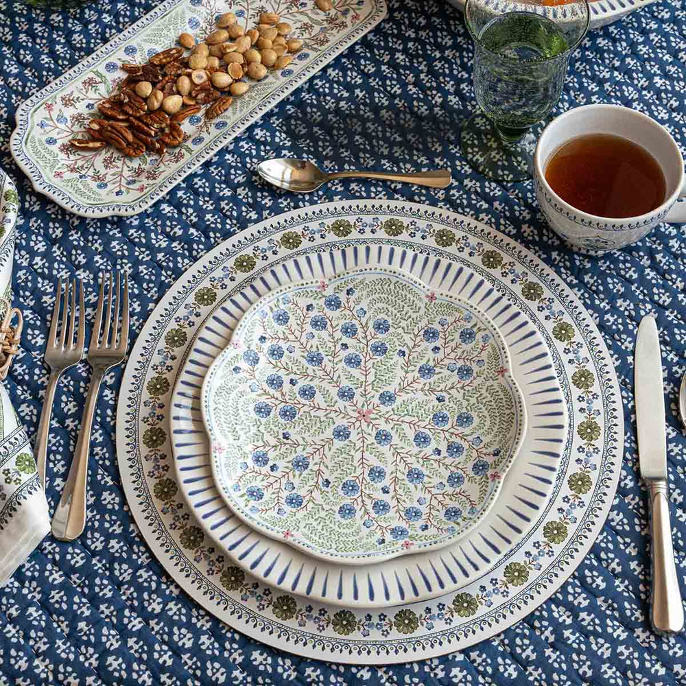 Table setting with layered patterned plates on a Seville green cork-backed placemat over a blue floral tablecloth