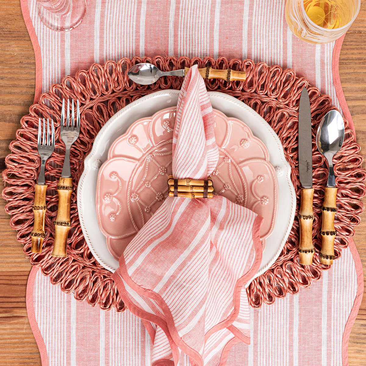 Top view of Straw Loop Oval Placemat in Coral showcasing handwoven looped edges with a styled table setting